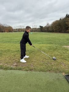 Jeugdgolfer staat klaar om een bal te slaan op de driving range, geconcentreerd in de setup met driver op een grasafslag.