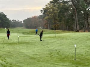 Jeugd golfers oefenen putten op de putting green van een bosrijke golfbaan.